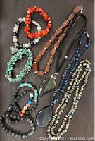 Four necklaces and six stretchy bracelets displayed on a dark fabric background. Includes coral, turquoise, onyx, and other semi-precious stones in varied shapes such as chips and chunky beads.