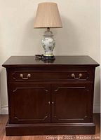 Solid mahogany cabinet with drawer and two doors, brass hardware, shown with table lamp on top.
