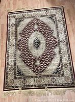 Full view of the rectangular rug showing detailed maroon and cream patterns with central medallion and tassels at one end.