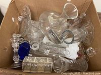 View of mixed crystal and glassware including candleholders, vases, bowls, napkin rings and decorative items in a cardboard box.
