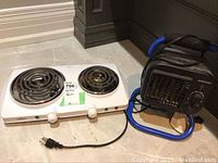 Image of white Walton 2 burner electric hot plate with coil burners and black Mastercraft portable heater with blue handle tube.