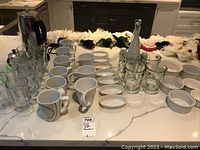 The full set displayed on a kitchen countertop showing mugs, ramekins, espresso pot, coffee maker, and condiment set.