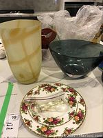Lot of three items on kitchen counter: yellow swirled glass vase, dark tinted glass bowl, floral patterned plate with roses