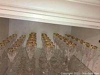 Photo showing the rows of crystal glasses with gold rims arranged on a shelf, three distinct sizes visible.