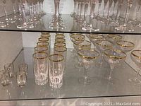 Shelves filled with etched crystal glasses featuring gold rims, showing arranged shot glasses, tumblers, and champagne glasses.