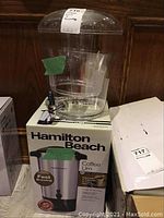 Hamilton Beach branded coffee urn box and large clear plastic beverage dispenser on top of box.