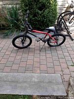 Side view of the red and black BMX style bike on a brick patio, showing frame and tires