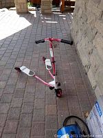 Pink and white Flicker ride-on scooter with black rubber hand grips, white foot platforms with gray grip pads, and three wheels.