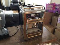 Front view of stainless steel Lavazza Espresso Point machine with gold-tone accents on wooden table