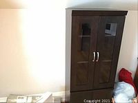 Front angled view of the tall dark wood cabinet with glass doors and visible scratches.