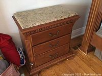 Front view of wooden night table with granite top and three drawers, shows carved details and antique metal handles.