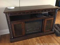Electric fireplace in wooden mantel, unpowered, showing front view with glass cabinet doors and shelf above insert.