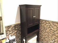 Full view of brown wooden over the toilet cabinet against the wall above the toilet showing the entire cabinet from top to bottom.