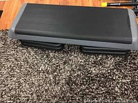 Top view of the exercise step platform showing the black textured surface and risers underneath.