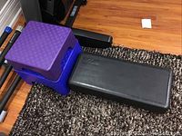 Photo of two purple/blue exercise steps stacked and one large black Bally exercise step on carpeted floor