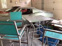 Photo of patio table and three turquoise mesh chairs set in outdoor or garage space with a silver car in background.