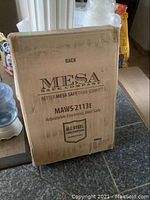 Photo of sealed cardboard box of Mesa Safe Company MAWS-2113E adjustable electronic wall safe, showing printed product and brand information.