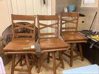 Photo showing three wooden counter height swiveling stools with crossbar backrests positioned in a garage area.