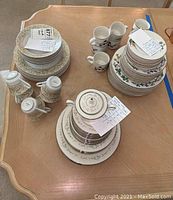 Photo showing three china sets on wooden table with plates, cups, teapot and shakers