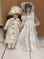 Two porcelain dolls side by side for size and detail visibility, showing full outfits from head to toe.