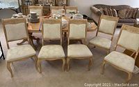 Set of 8 wooden dining chairs arranged in two rows showing cream colored upholstered seats and backs with carved wooden frames.