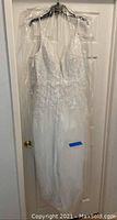 Full view of white wedding dress hanging on door in plastic garment bag