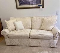 Front view of cream beige couch with four decorative pillows in light tone upholstery against a white wall.
