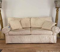 Front view of cream-colored upholstered couch with two matching throw pillows, showing the fabric pattern and structure