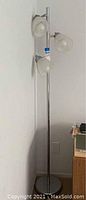Full view of the tall silver floor lamp with three white glass shades attached vertically on the pole.