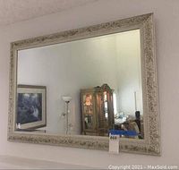 Front view of large rectangular decorative mirror hanging on wall, showing clear reflective surface and carved frame detail