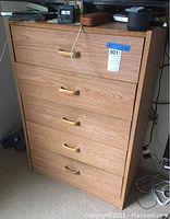 Front view of the wooden dresser showing five drawers with curved wooden handles and some items on top.