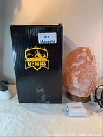 Photo showing Himalayan salt lamp next to original black box with DRMNS label and two small boxes likely containing bulbs.