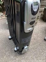 Side view of the black DeLonghi oil heater showing fins and power cord wrapped around holders, on caster wheels.