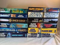 Lot of 12 hardcover Clive Cussler novels stacked in two columns, titles clearly visible for identification.