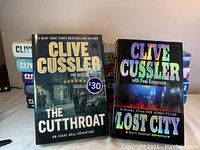 Front covers of two Clive Cussler novels visible: 'The Cutthroat' and 'Lost City' showing condition and dust jackets