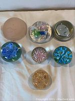Top view showing all seven assorted paperweights of various styles and sizes on a white surface.