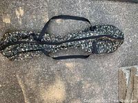 Front view of long, narrow army camouflage hoverboard bag with zipper and handles laid flat on pavement.