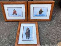 Three framed prints of Inuit children in snow, oak and wood frames, double matted, showing one child alone or with dog