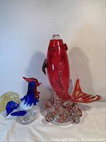 Photo showing the full lot with the red koi fish and the multicolored rooster glass figurines on a white background