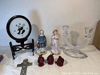 View of porcelain panda plate, two figurines, three red figurines, metallic cross, and glass candlestick holder.