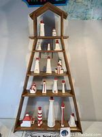 Front view of wooden tiered image frame containing multiple white and red lighthouse figurines on four shelves