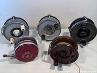 Top-down view of five fishing reels showing two gray Windex reels, red Castrite reel, brown Alpha reel, and black South Bend reel.