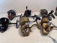 Lot of six vintage casting reels, various brands and styles visible, arranged on a white cloth surface.