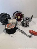 Overall view of assorted fishing reels and fishing line spools on white surface.