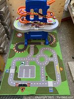 Full setup of Step2 car track on a road play mat with toy cars on and around the track.