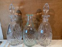Front view of two crystal pineapple design decanters with lids and one clear glass decanter no lid, all standing upright.