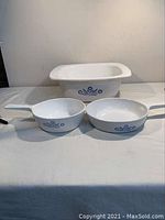 Three white glass Pyrex cookware pieces on a white cloth surface with blue cornflower design visible.