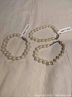 Three pearl bracelets laid out, showing uniform 8mm pearls and silver-tone clasps.