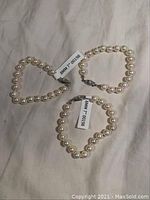 Three pearl bracelets displayed on a fabric surface, showing uniform size pearls and circular shape.