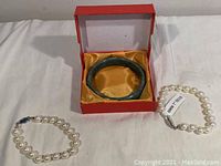 Photo showing jade bangle bracelet inside red gift box with satin lining, along with two pearl bracelets laid out on a white surface.